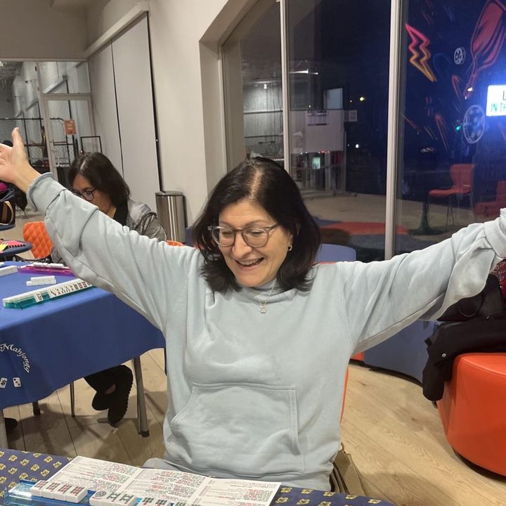 A JEM member celebrating with both arms wide at a Mahjong table